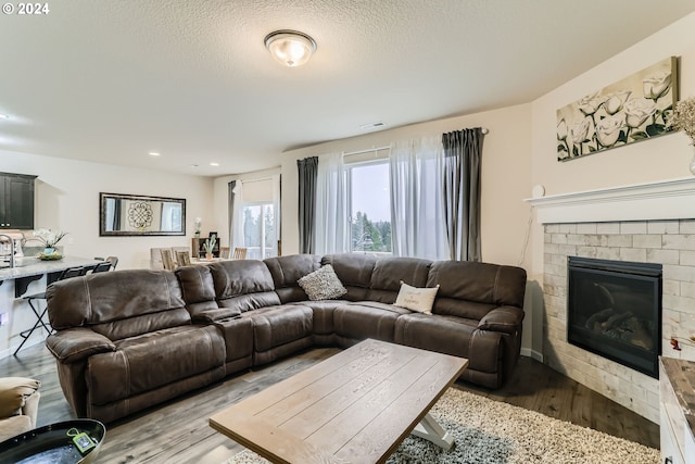 living room featuring light wood-type flooring, a textured ceiling, and a fireplace