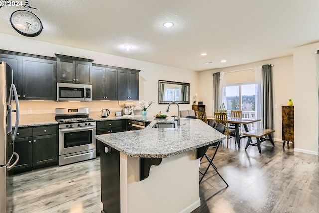 kitchen with a breakfast bar, sink, stainless steel appliances, light stone countertops, and light hardwood / wood-style flooring