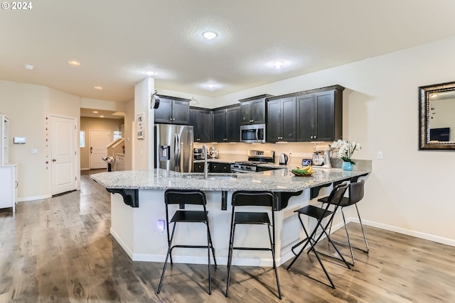 kitchen featuring sink, a kitchen bar, light stone counters, kitchen peninsula, and stainless steel appliances