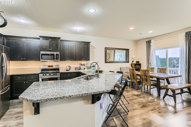 kitchen with stainless steel appliances, sink, a breakfast bar, and light wood-type flooring