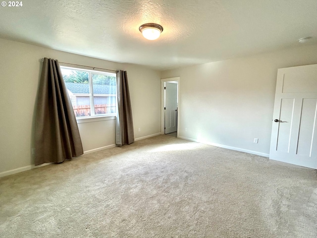 empty room with baseboards, a textured ceiling, and light colored carpet