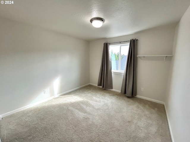 empty room featuring light colored carpet, a textured ceiling, and baseboards