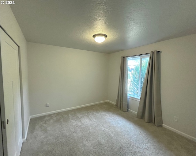 unfurnished room with light carpet, a textured ceiling, and baseboards