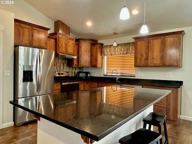 kitchen featuring a breakfast bar area, decorative light fixtures, a center island, stainless steel appliances, and under cabinet range hood