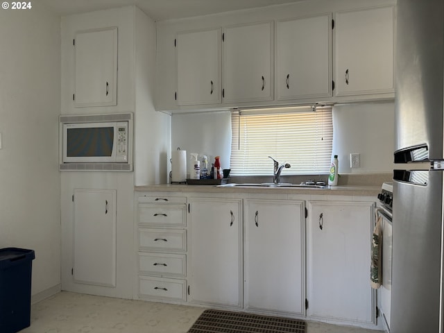 kitchen featuring stainless steel fridge, white microwave, white cabinetry, and sink