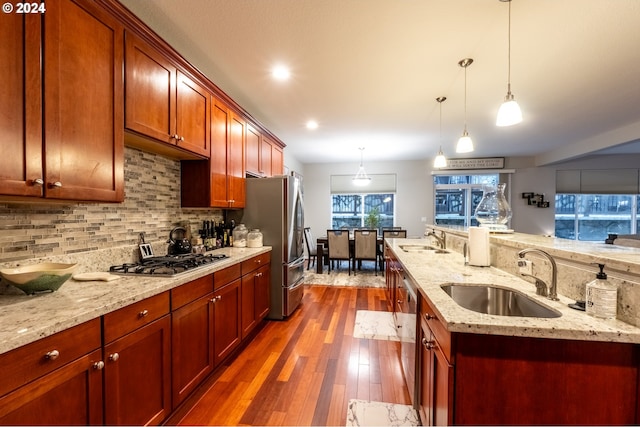 kitchen with tasteful backsplash, dark hardwood / wood-style floors, light stone countertops, hanging light fixtures, and sink