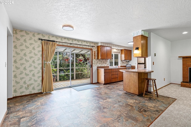 kitchen with a textured ceiling, a kitchen breakfast bar, a fireplace, and kitchen peninsula