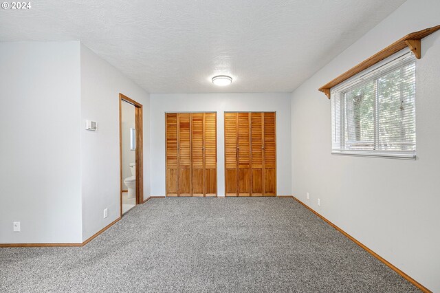 unfurnished bedroom with two closets, a textured ceiling, ensuite bathroom, and carpet flooring