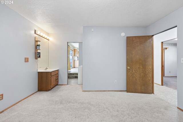 carpeted bedroom featuring a textured ceiling, ensuite bathroom, and sink