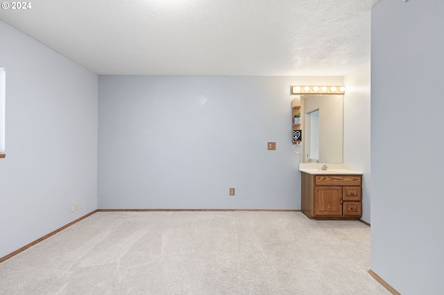 unfurnished bedroom with a textured ceiling, sink, light carpet, and ensuite bathroom