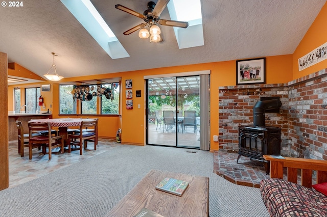 carpeted living room featuring ceiling fan, a wood stove, and lofted ceiling with skylight