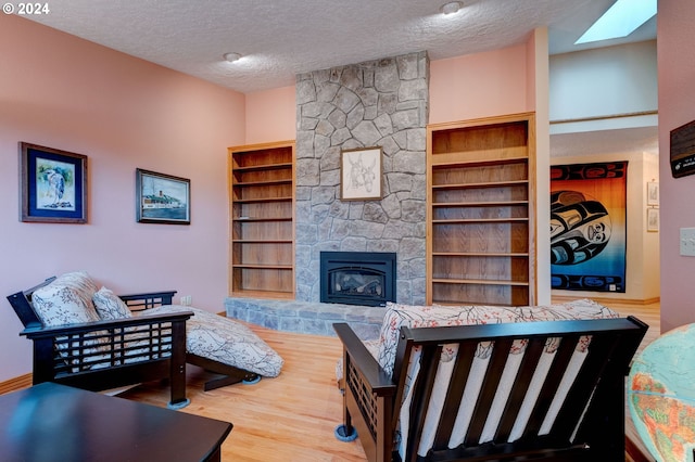 living room with a textured ceiling, built in shelves, and a stone fireplace