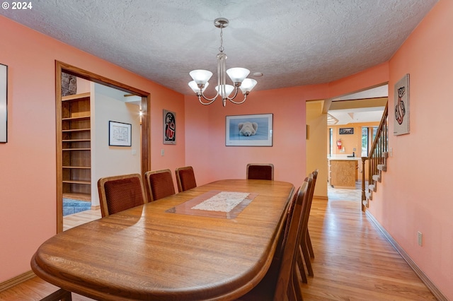 dining area with light hardwood / wood-style floors, a textured ceiling, built in features, and an inviting chandelier