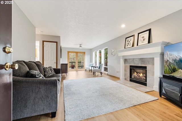 living room with a textured ceiling, ceiling fan, light wood-type flooring, and a fireplace