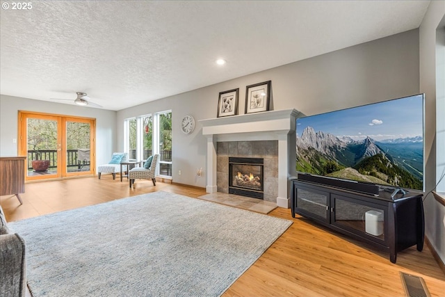 living room with a tile fireplace, ceiling fan, light hardwood / wood-style flooring, and a textured ceiling