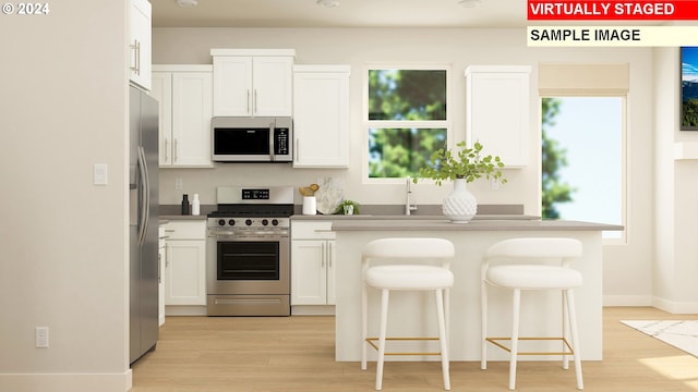 kitchen with light wood-type flooring, a kitchen breakfast bar, a wealth of natural light, stainless steel appliances, and white cabinets