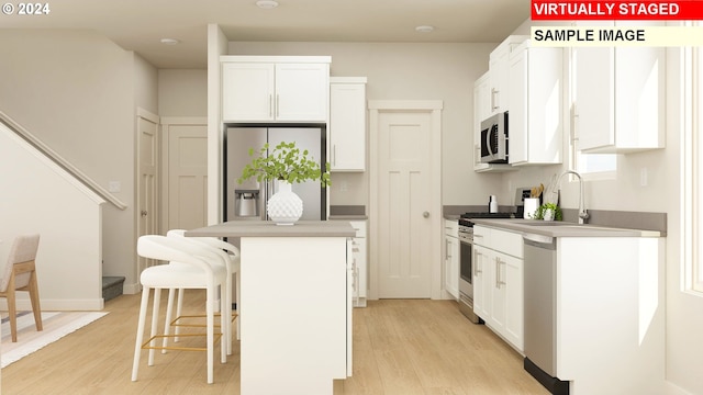 kitchen with stainless steel appliances, a center island, white cabinets, a kitchen bar, and light wood-type flooring