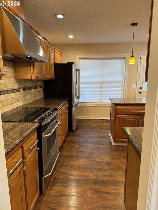 kitchen with dark hardwood / wood-style flooring, dark stone counters, wall chimney exhaust hood, stainless steel range oven, and hanging light fixtures