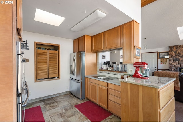 kitchen featuring kitchen peninsula, a skylight, black electric cooktop, light stone countertops, and stainless steel refrigerator with ice dispenser