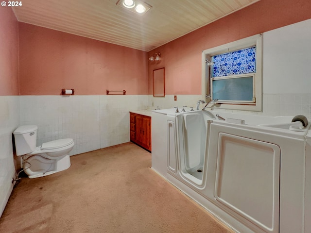 bathroom with tile walls, independent washer and dryer, vanity, a tub to relax in, and toilet