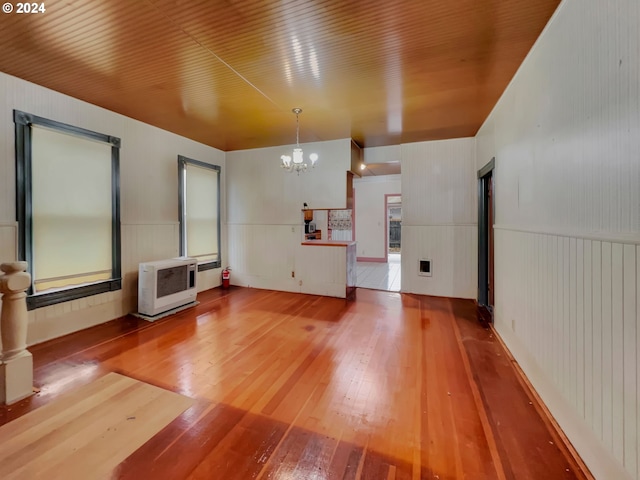 unfurnished living room with heating unit, a notable chandelier, and hardwood / wood-style flooring