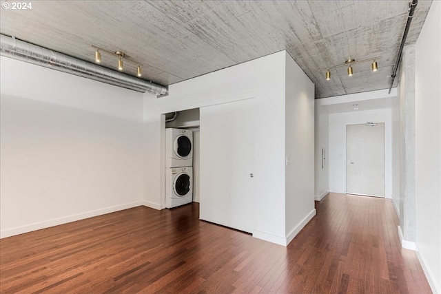 laundry room featuring stacked washer / dryer, dark hardwood / wood-style flooring, and track lighting