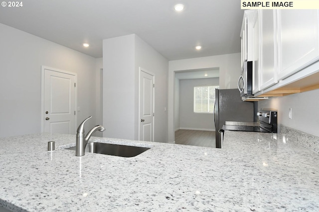 kitchen with light stone countertops, stove, sink, hardwood / wood-style flooring, and white cabinetry