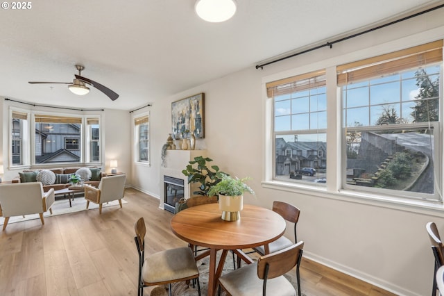 dining area with a tile fireplace, light hardwood / wood-style floors, and ceiling fan