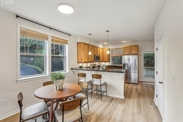 kitchen with appliances with stainless steel finishes, decorative light fixtures, a kitchen bar, kitchen peninsula, and light hardwood / wood-style flooring