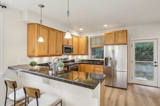 kitchen with kitchen peninsula, pendant lighting, light hardwood / wood-style flooring, a kitchen bar, and stainless steel appliances