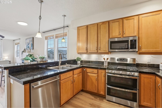 kitchen with kitchen peninsula, appliances with stainless steel finishes, sink, decorative light fixtures, and light wood-type flooring