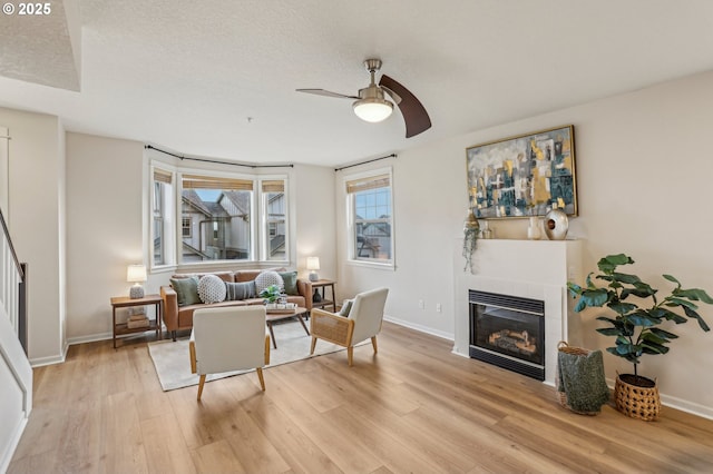 living room with ceiling fan, a textured ceiling, light hardwood / wood-style floors, and a fireplace