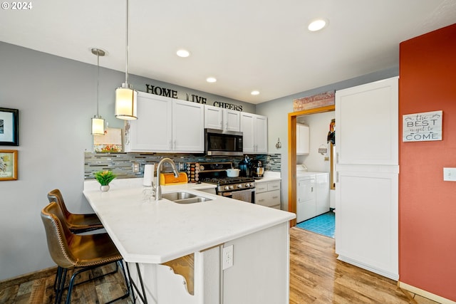 kitchen featuring white cabinetry, sink, kitchen peninsula, appliances with stainless steel finishes, and independent washer and dryer