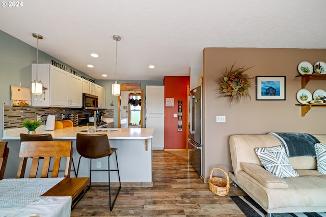 kitchen featuring appliances with stainless steel finishes, hanging light fixtures, hardwood / wood-style flooring, a kitchen breakfast bar, and kitchen peninsula