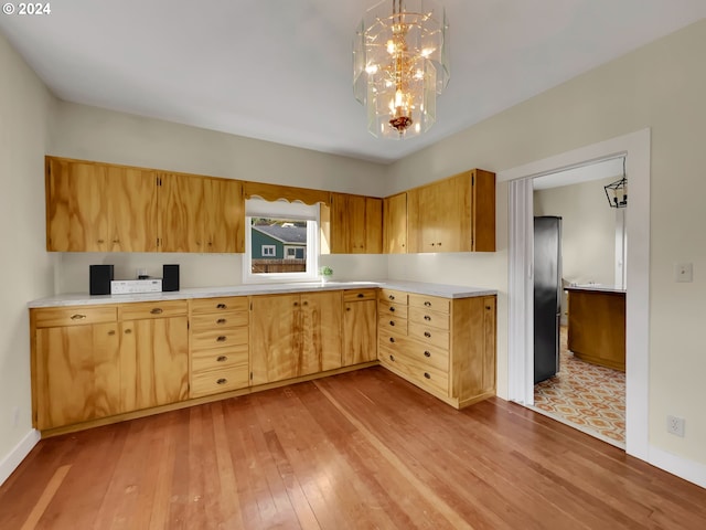 kitchen featuring light hardwood / wood-style floors, stainless steel refrigerator, pendant lighting, sink, and a notable chandelier