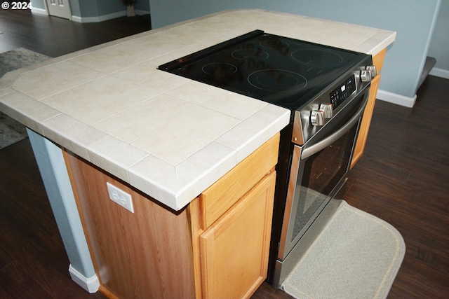 kitchen view of stainless steel electric range oven, baseboards, dark wood-style floors, and tile countertops