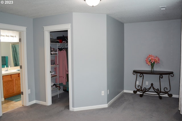 bedroom with a spacious closet, carpet flooring, a closet, a textured ceiling, and baseboards