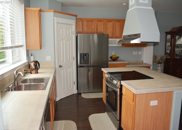 kitchen with appliances with stainless steel finishes, a sink, tile counters, island range hood, and dark wood-type flooring