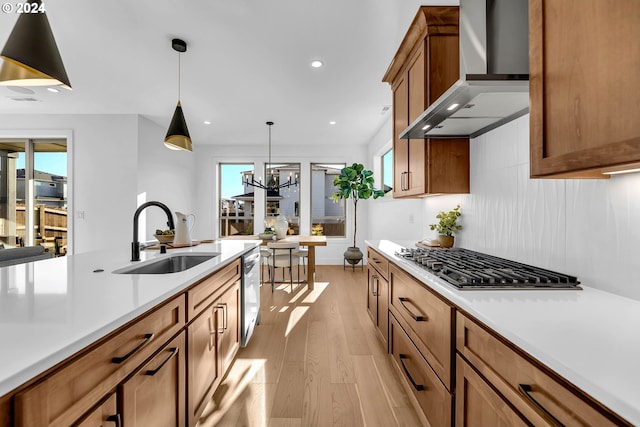 kitchen featuring sink, wall chimney exhaust hood, light wood-type flooring, appliances with stainless steel finishes, and decorative light fixtures