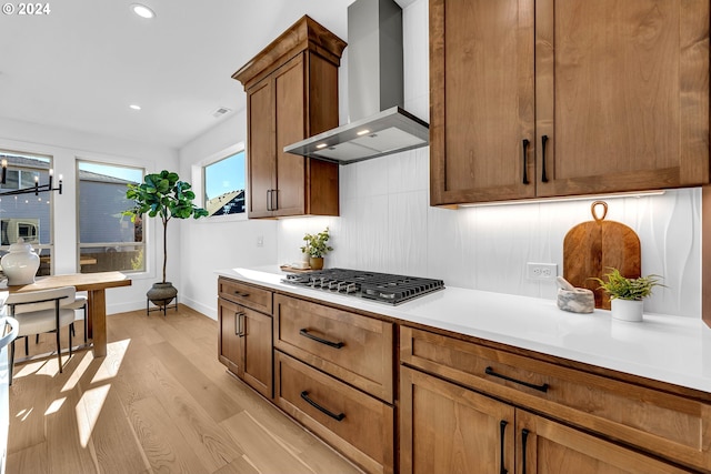 kitchen with tasteful backsplash, light hardwood / wood-style flooring, wall chimney range hood, and stainless steel gas cooktop