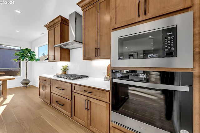 kitchen featuring light hardwood / wood-style floors, wall chimney range hood, and appliances with stainless steel finishes