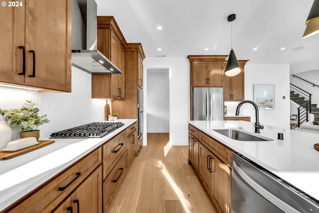 kitchen featuring sink, wall chimney exhaust hood, light hardwood / wood-style flooring, pendant lighting, and appliances with stainless steel finishes