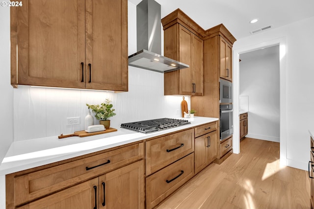 kitchen with stainless steel appliances, wall chimney range hood, and light hardwood / wood-style floors