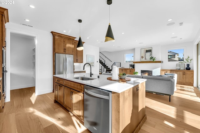 kitchen featuring a healthy amount of sunlight, an island with sink, light wood-type flooring, and appliances with stainless steel finishes