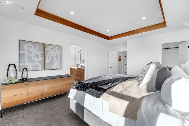 bedroom featuring ensuite bathroom, dark carpet, and a raised ceiling