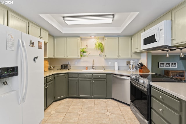 kitchen featuring light tile patterned flooring, appliances with stainless steel finishes, a tray ceiling, and a sink