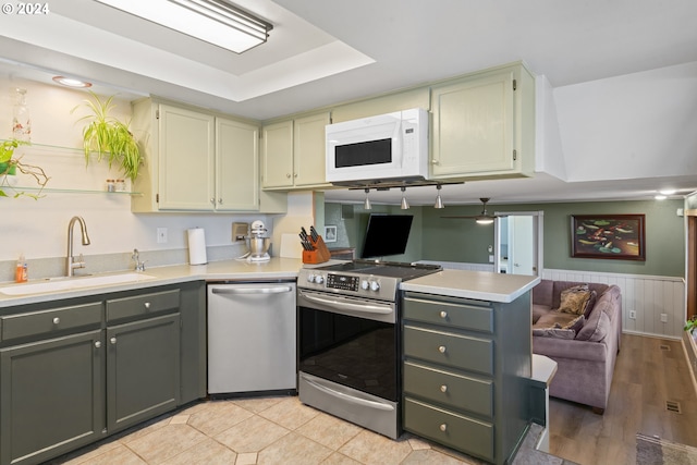 kitchen with a wainscoted wall, a sink, appliances with stainless steel finishes, a peninsula, and light countertops