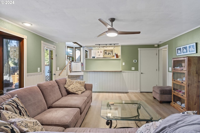 living area with a wainscoted wall, ornamental molding, wood finished floors, rail lighting, and ceiling fan