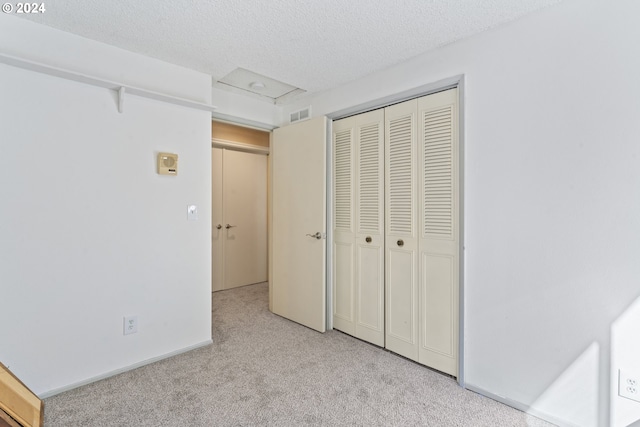 unfurnished bedroom with carpet, visible vents, attic access, a closet, and a textured ceiling