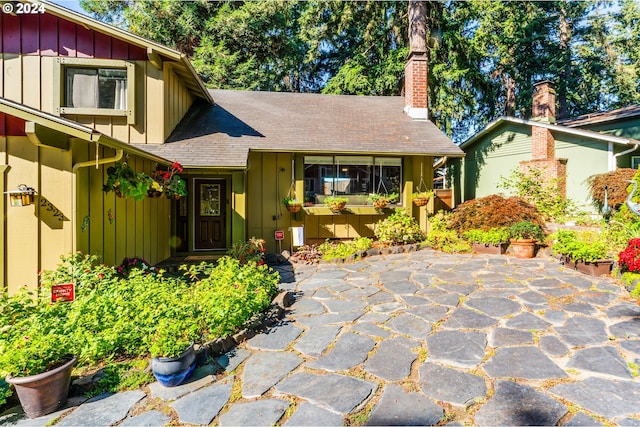 view of front facade with board and batten siding, a shingled roof, a chimney, and a patio area